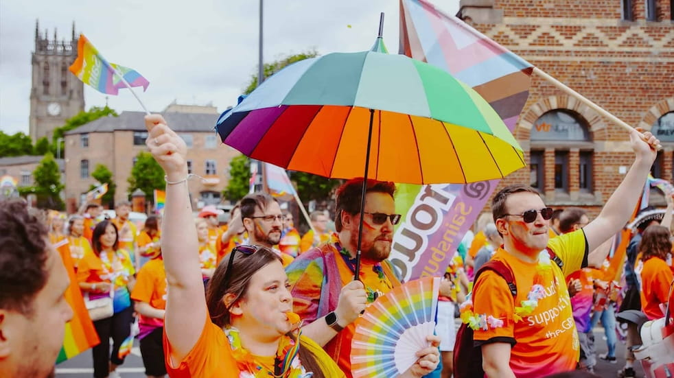 Attendees of Leeds' Pride Parade wearing bright colours and waving Pride flags
